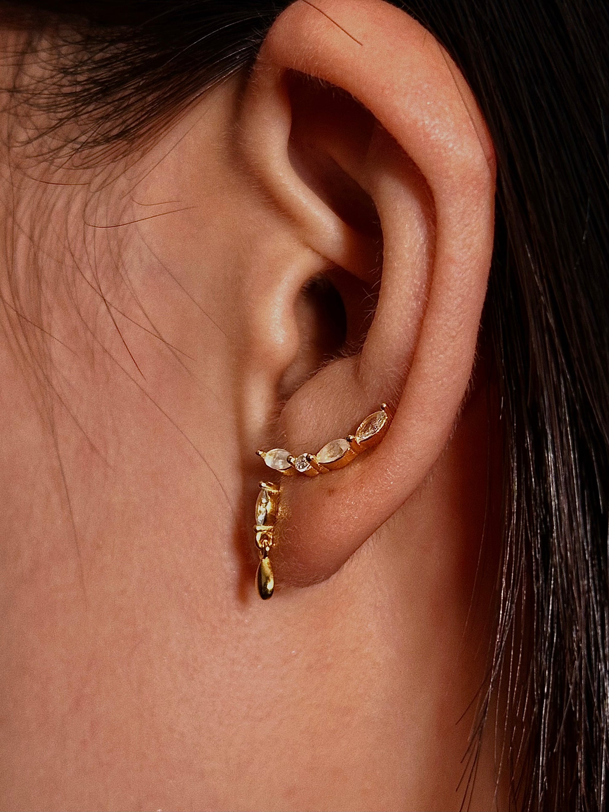 Natural moonstone curve flatback earring in 18K gold plated sterling silver, worn on earlobe, showcasing the stone's adularescent glow.